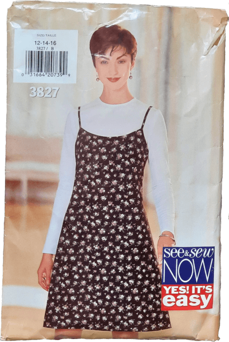 A photo of a sewing pattern for a sleeveless dress with thin straps made of a black fabric with small pink and white flowers on it. She is wearing a white long sleeve t-shirt underneath.