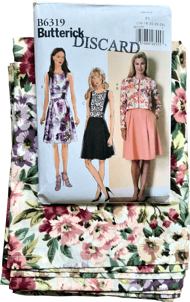 A photo of a sewing pattern with fabric laid underneath. The pattern shows 3 sleeveless dresses. The fabric is cream-coloured with pink, tan, and purple flowers on it.